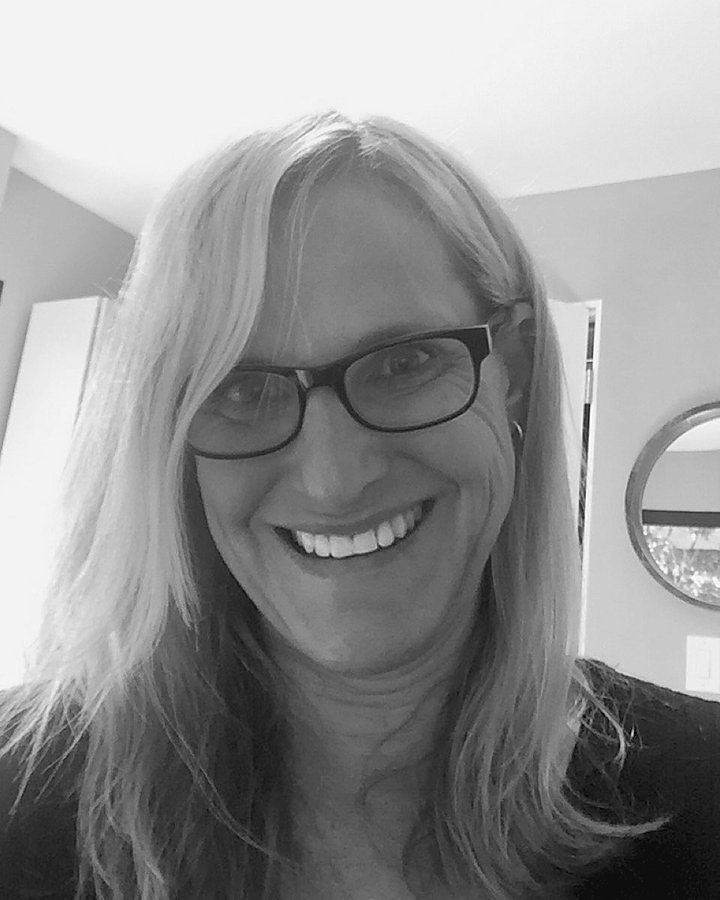 Black and white portrait of Sue Randall in glasses, smiling, at home